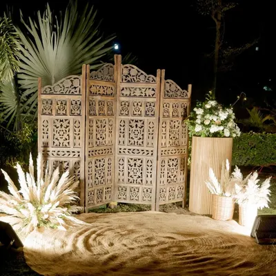 A perfect rustic photo booth for an evening event. We used a carved wooden screen, jute flooring, pampas grass arrangements, and warm spotlights to create this cozy corner.