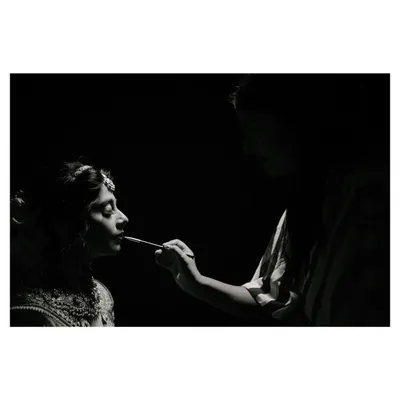 A timeless black and white portrait capturing the final touches of the bride's makeup. The dramatic lighting highlights the quiet focus and anticipation in the room, creating an artistic and intimate getting ready shot.