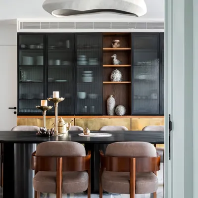 Storage is key in any family home, and these wall cabinets with fluted glass and brass shutters offer both style and function. A bespoke wooden niche showcases curated artifacts, complementing the warm glow of the suspended light.
