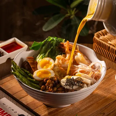 The moment a rich, steaming broth is poured over a bowl of ramen, bringing all the ingredients together.