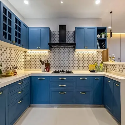 A beautiful U-shaped kitchen in a classic shaker style, painted in a calming shade of blue. The design is complemented by a patterned backsplash, white countertops, and elegant brass handles, creating a timeless and inviting space.