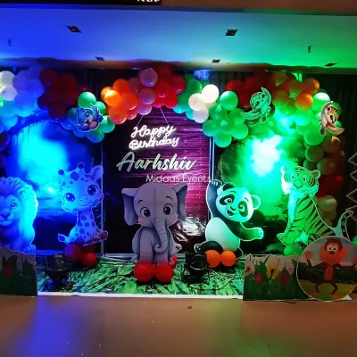 A wide view of the complete jungle safari theme setup for Aarshiv's birthday. The decor features a full balloon arch, a personalized neon sign, and multiple cute animal cutouts like a lion, giraffe, elephant, and panda.