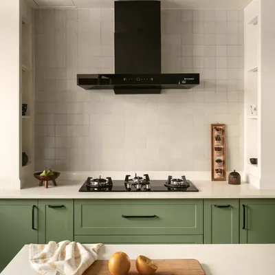 The gorgeous kitchen in the Earthy Hacienda home features sage green cabinets and a hooded cooktop with built-in niches for spices. The design is elevated by thoughtful details that enhance both aesthetics and functionality.