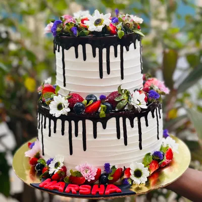 A beautiful two-tier mixed berry cake. This non-chocolate option is a showstopper, featuring a dark chocolate drip and adorned with fresh strawberries, blueberries, and edible flowers.