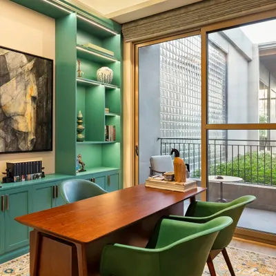 Not all workspaces need to be behind closed doors. This vibrant home office uses a bold teal for the built-in shelving, creating an inspiring and energetic atmosphere. The desk overlooks a green courtyard, providing a connection to nature throughout the workday.