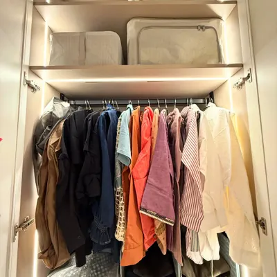 A well-lit wardrobe where clothes are hung neatly above, and seasonal items are stored in matching bags on the top shelf. This is a great example of using vertical space effectively.