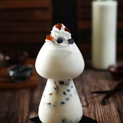 A whimsical mushroom-shaped glass filled with a creamy boba drink. The dark, woody background and moody lighting create a magical, forest-like atmosphere that makes the drink feel unique and enchanting.