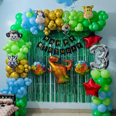 A fun jungle-themed birthday arch for a 3-year-old. This decoration features green, blue, and gold balloons, a green tinsel backdrop, and lots of animal foil balloons like a monkey, zebra, and dinosaur.