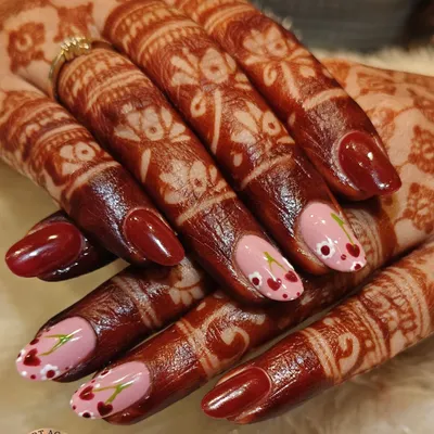 This beautiful bridal manicure combines rich maroon nails with delicate, hand-painted cherry blossom art on a soft pink base. The design perfectly complements the intricate mehndi, creating a look that balances tradition with modern elegance.