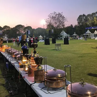 An outdoor buffet line set against a beautiful sunset. Our team arranges everything to perfection, using decorative lanterns and traditional copper serveware to create a magical dining experience on the open lawn.