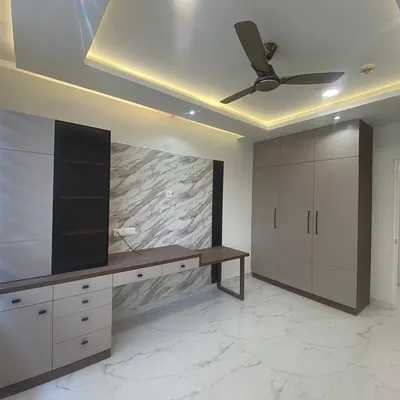 This bedroom combines a built-in wardrobe with an integrated study desk against a marble-textured wall panel. The design is both space-efficient and stylish.