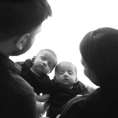 An artistic black and white shot from above, showing parents looking down at their twin babies. The reflection creates a beautiful and symbolic image of the new family.
