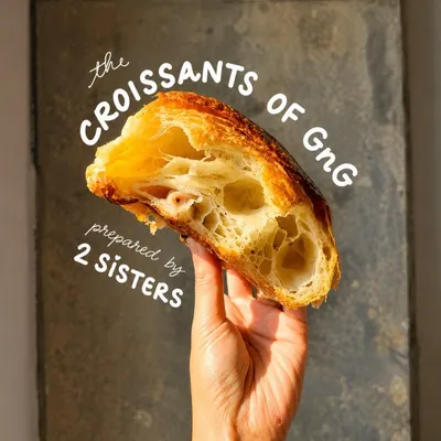 A torn croissant shows its layers in our bakery display, with the sisters' croissant collection named above it.