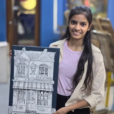A proud student holds her completed micron pen drawing, an incredibly detailed illustration of a storefront that showcases her patience and precision with ink.