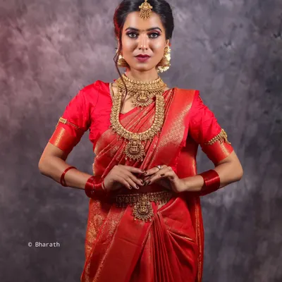 A full-length studio portrait of a model in a stunning red Kanjivaram silk saree. The focus is on the complete bridal look, from the temple jewelry and waist belt (vaddanam) to the traditional drape of the fabric.