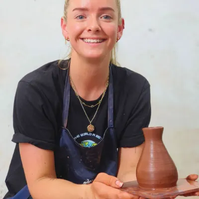 A smiling traveler from abroad proudly holds up the vase she made in our workshop. We are honored to welcome visitors from around the world to experience Indian art and culture firsthand.