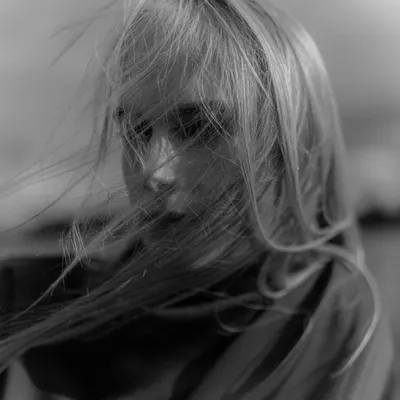 A soft-focus black and white film portrait, where the wind blows the model's hair across her face, creating a sense of movement and emotion.
