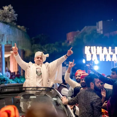 A groom making a rockstar entrance for his baraat, standing on top of a car, ready to celebrate.