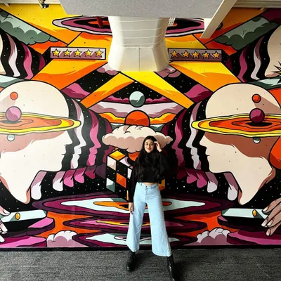 Here I am with the completed customer service-themed mural at the Rippling office. It's incredibly rewarding to see a digital design come to life at this scale.