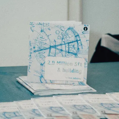 A photo of the book "2.9 Million Sft & building" by Sridevi Adlakha, which chronicles the personal and professional journey of our firm. The cover features a blueprint sketch, symbolizing our deep roots in the architectural process.