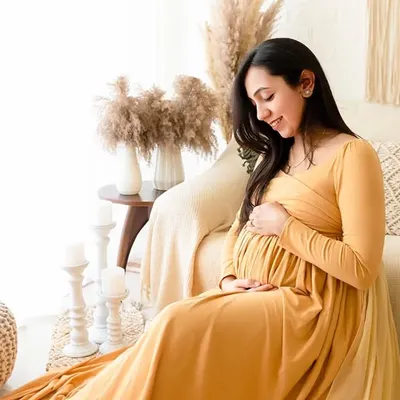 A solo maternity portrait in a mustard yellow gown, set against a bright, boho-chic studio setup. The natural light and earthy decor elements create a warm and inviting atmosphere.