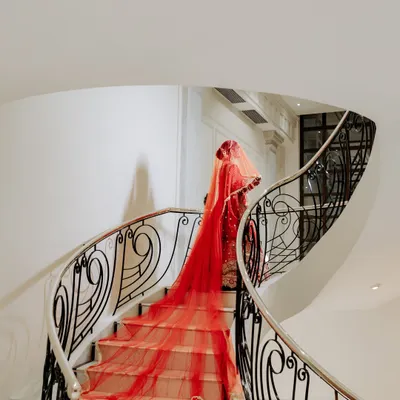 A bride's descent down a spiral staircase, her magnificent red veil trailing behind her. This is a portrait of pure drama and elegance, a fairytale moment brought to life.