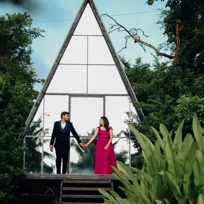 Holding hands before their new beginning. This shot at a Bangalore studio highlights the couple against the modern glass structure, with the lush greenery framing them perfectly. It's a classic romantic pose with a contemporary feel.