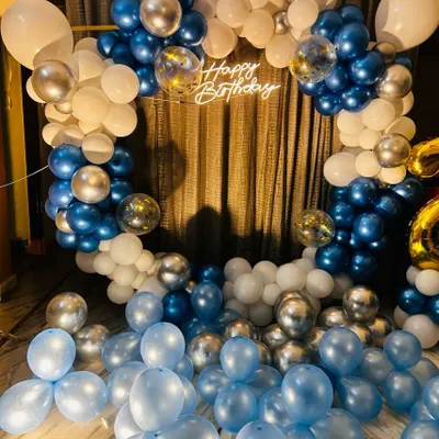 A classic home birthday decoration featuring a full ring balloon arch in blue, white, and silver chrome. The 'Happy Birthday' sign in the center and balloons scattered on the floor create a festive and immersive feel.