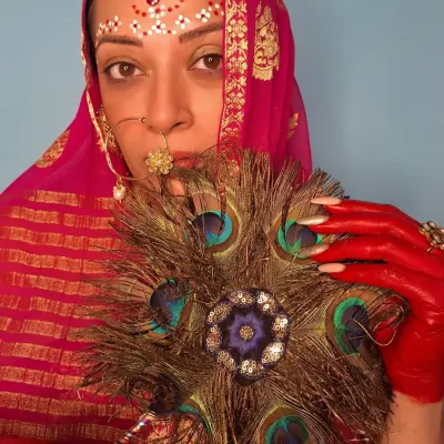 A conceptual look inspired by Radha for Janmashtami. The styling involves traditional elements like a pink bandhani dupatta, a maang tikka, and a nath, but with an artistic twist: the hands are painted with red alta, and the forehead has intricate bindi art.