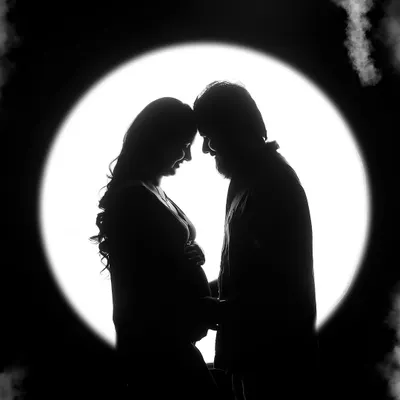 A stunning maternity silhouette of a couple against a circular light source. This artistic black and white photo creates a feeling of intimacy and wonder.