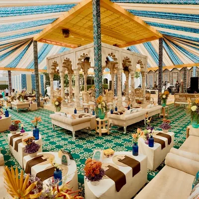 An overview of the 'Rang Mahal' welcome lunch, showcasing the grand tented structure with its striped canopy. The central bar, made of carved stone, and the surrounding plush lounges create a space that is both regal and inviting.