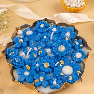 A close-up of a stunning blue floral candle, highlighting the intricate details of the wax flowers and gold leaf accents.