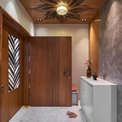The front door is the first handshake of your home. I designed this entrance with a combination of vertically fluted wood, a custom circular handle, and a glass insert, all under a ceiling with a beautiful floral detail.