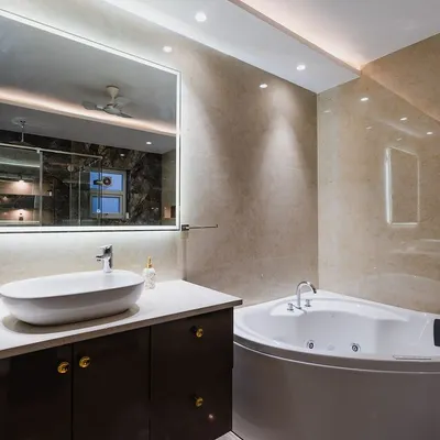 This bathroom design blends elegance and modernity. It features a corner jacuzzi tub, a sleek vanity with a vessel sink, and an illuminated mirror, all set against warm beige marble tiles.