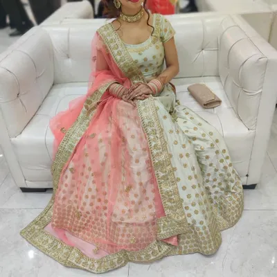 A client seated comfortably in our pista green lehenga with a peach dupatta. The gold butti work on the skirt and the embroidered border make it a graceful choice for any wedding guest.