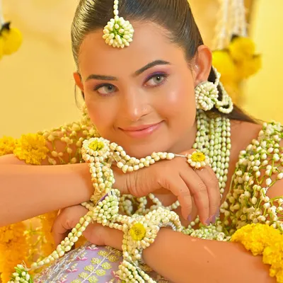 A close-up of a beautiful bride adorned in fresh floral jewelry for her Haldi ceremony. The makeup is kept fresh and dewy with a hint of purple on the eyes to match her outfit.