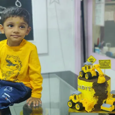 A young birthday boy sitting proudly next to his custom-made construction theme cake.