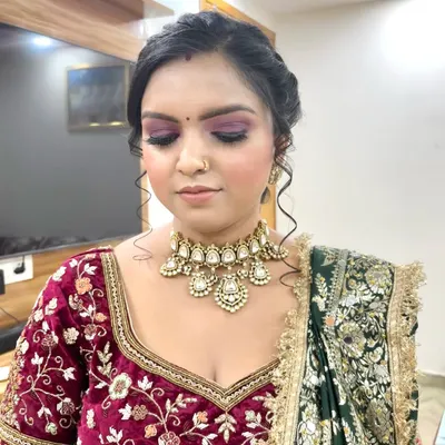 A close-up of a classic bridal look featuring a dramatic purple smokey eye and a neutral lip, perfectly complementing the rich velvet lehenga. The skin is kept radiant to catch the light beautifully.