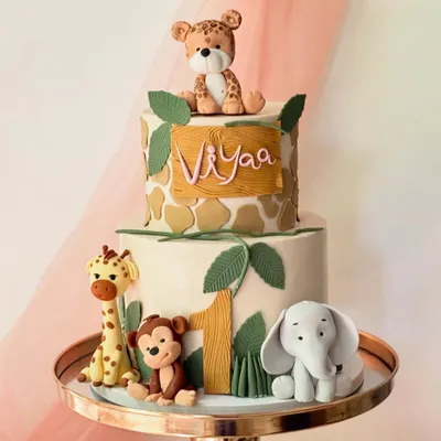 This two-tiered jungle safari cake is perfect for a first birthday. It features a giraffe-print top tier and fondant figures of a leopard, giraffe, monkey, and elephant.