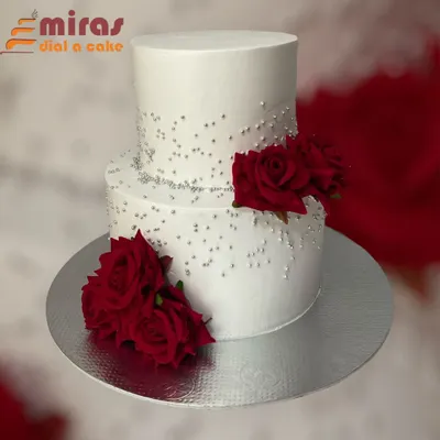 This elegant two-tier cake features a clean white buttercream finish, delicate silver beadwork, and deep red roses. It's a sophisticated choice for a formal corporate anniversary or celebration.