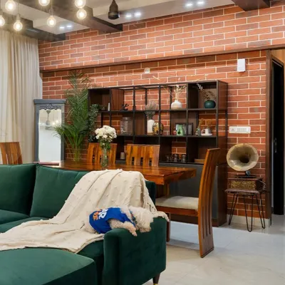 This industrial-chic living room features a raw brick accent wall, a deep emerald green sofa, and custom wood shelving. The space is a perfect mix of refined and rustic, with our puppy Cookie adding a touch of homeliness.