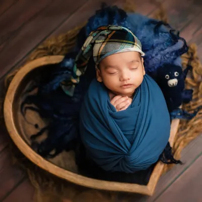 A sweet sleeping baby boy, snugly wrapped in blue and nestled in a heart-shaped bowl. This is a classic example of my posed studio newborn photography.