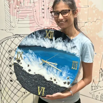 A student proudly holds up the gorgeous ocean-themed resin clock she created, complete with realistic waves and a textured sand effect.