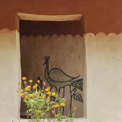 A detail from a vernacular homestay in Madhya Pradesh. The walls are finished with mud and decorated with a traditional peacock mural, framed by a pot of marigolds. This is architecture that celebrates local art and materials.