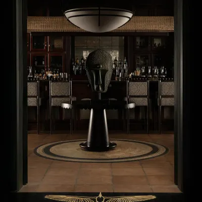 The entrance to Lord Elgin, where a sculptural mask stands as a modern artifact in a classical setting. The branded doormat and symmetrical composition create a formal and grand sense of arrival.