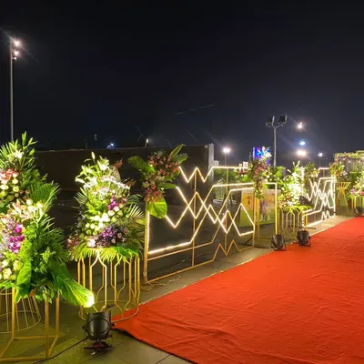A closer view of the red carpet entrance I designed for the ceremony honoring an Asian Games gold medalist. The path is flanked by modern, illuminated fixtures and vibrant floral displays on gold stands, creating a prestigious walkway.