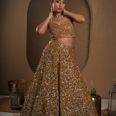 A full-body shot where the model looks directly at the camera, creating a powerful connection with the viewer. The lighting is set to make every sequin on the golden lehenga sparkle.