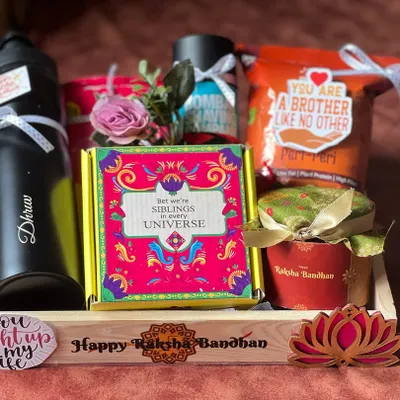 A personalized Rakhi hamper for a brother. This wooden tray includes a custom-engraved water bottle, snacks, and a quirky 'Siblings in every universe' box.