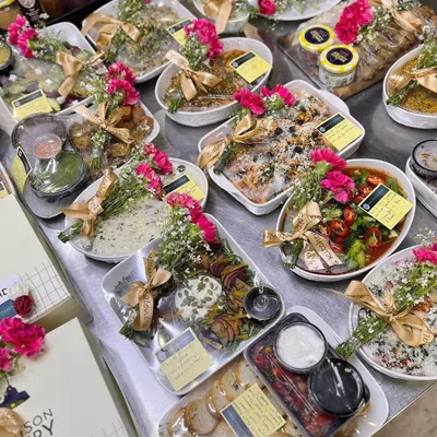This is my pre-plated meal gifting service, a perfect way to send love through food. This spread shows a variety of dishes, from salads and appetizers to main courses, all beautifully garnished with fresh flowers and ribbons.