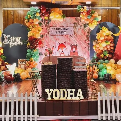 A whimsical woodland animal theme for Yodha's third birthday. This unique setup uses balloon trees, a white picket fence, and cute fox and owl characters to create an enchanting forest scene on stage.